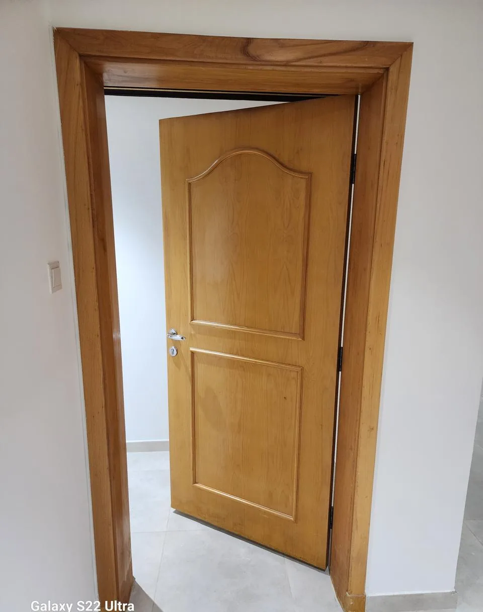 Natural wood panel door standing open in a timber frame