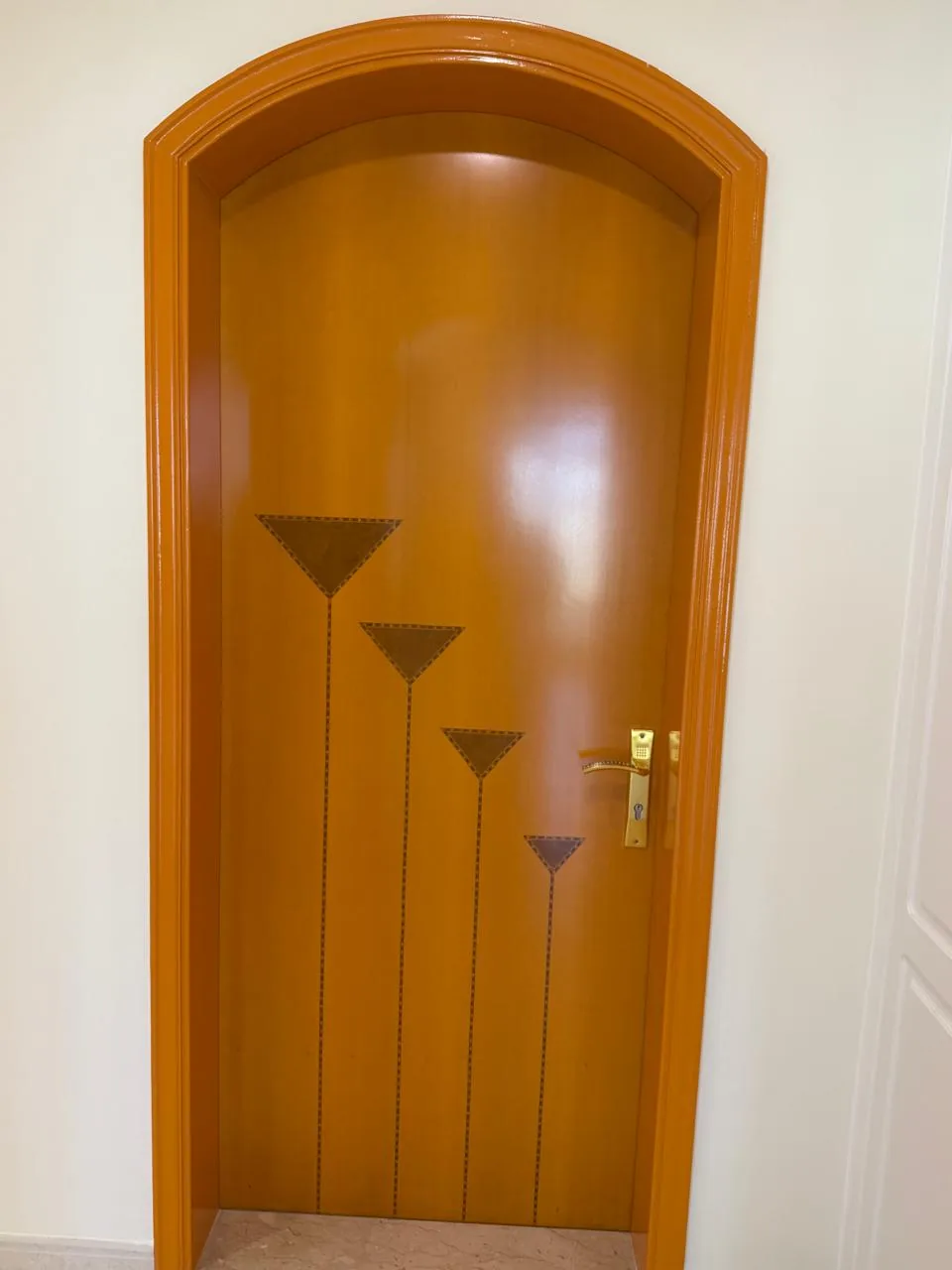 Arched wooden door with a tapered inlay design and a polished honey-wood finish
